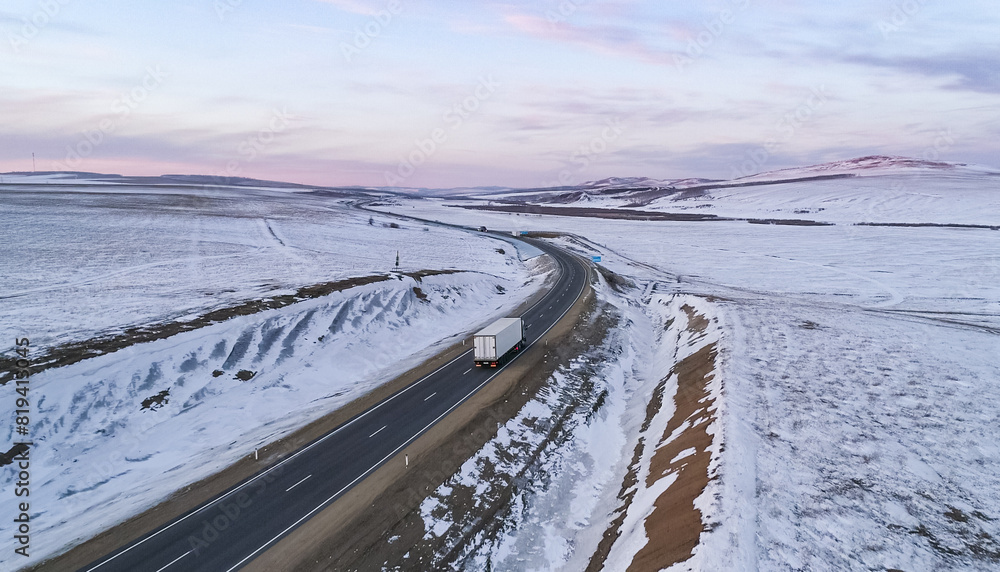 Lonely semi truck driving on snowy rural highway at dusk in winter landscape Lonely semi truck driving on snowy rural highway at dusk in winter landscape