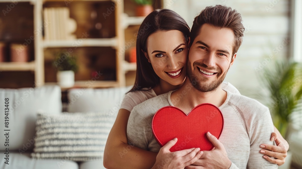 Young couple in love holding a heart shaped gift box in apartment