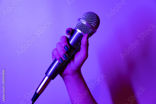 close-up shot of a hand holding a microphone in purple and pink lights