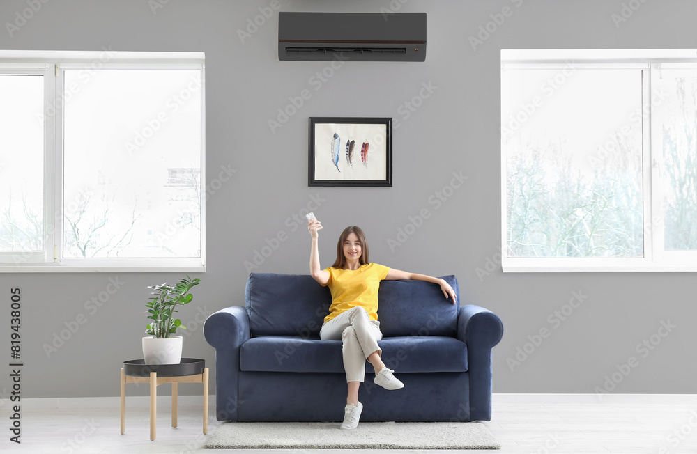 Young woman with air conditioner remote control at home Young woman with air conditioner remote control at home