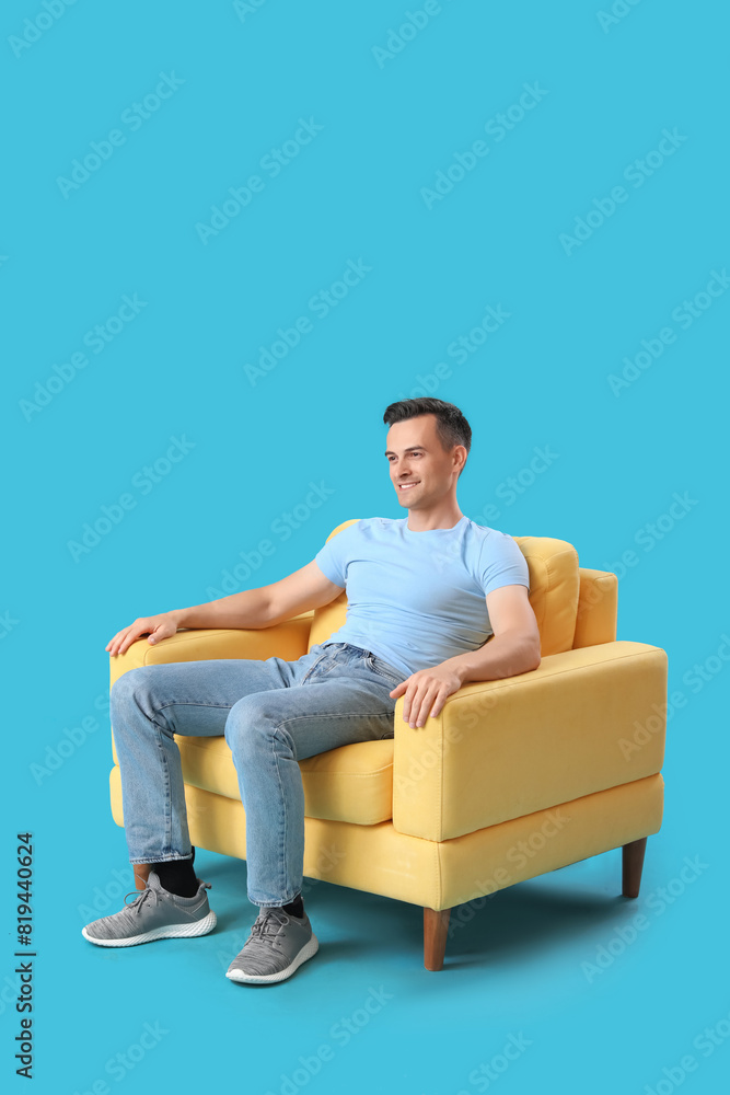 Handsome man sitting in yellow armchair on blue background Handsome man sitting in yellow armchair on blue background
