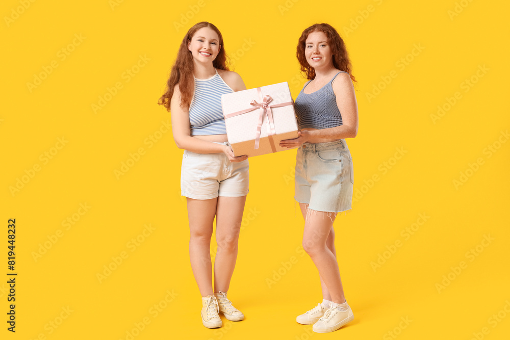 Happy redhead sisters with gift box on yellow background Happy redhead sisters with gift box on yellow background