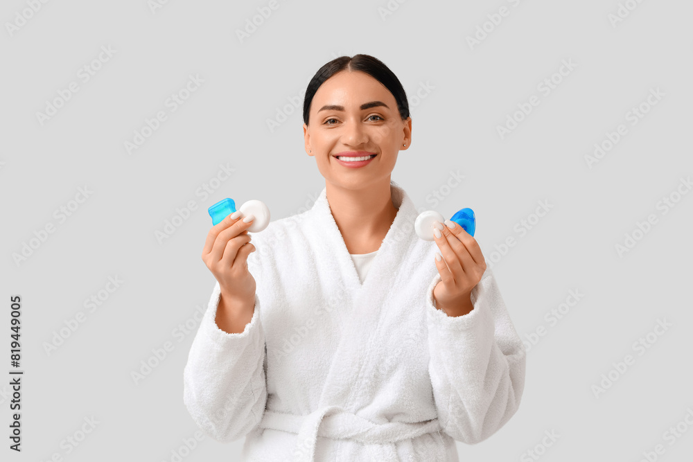 Beautiful young happy woman in bathrobe with different dental floss on grey background Beautiful young happy woman in bathrobe with different dental floss on grey background