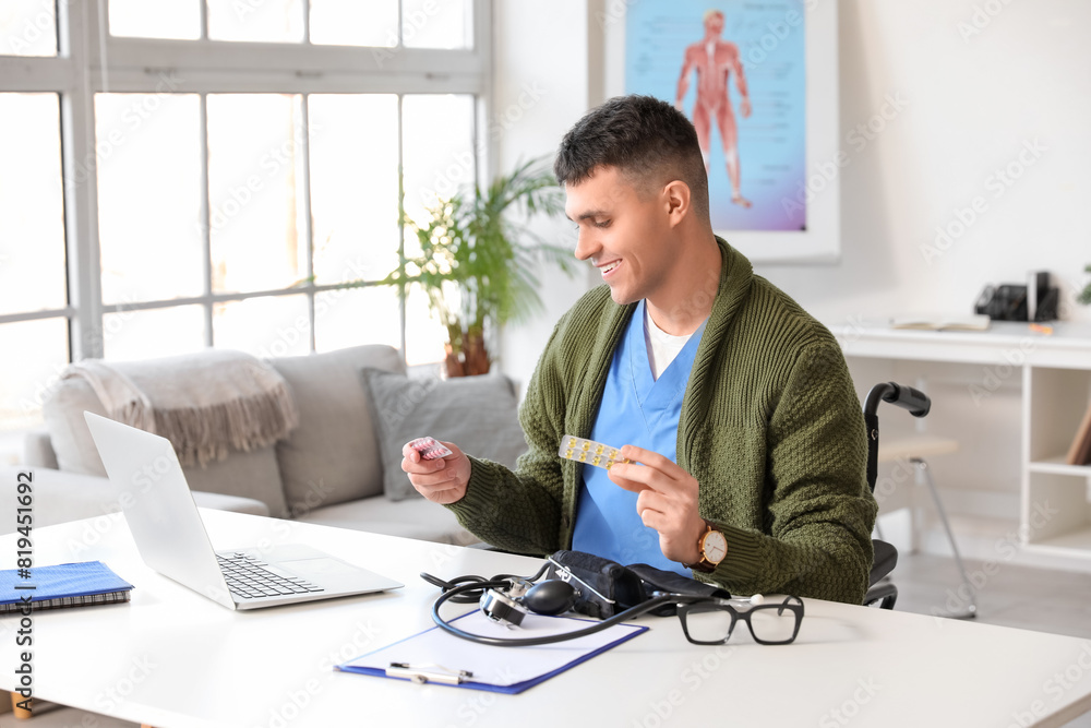 Young male doctor in wheelchair with pills working at his workspace in clinic Young male doctor in wheelchair with pills working at his workspace in clinic