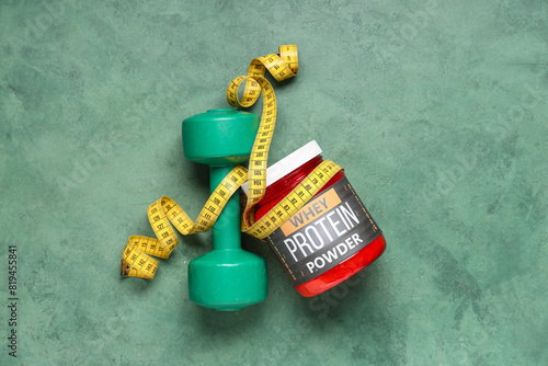 Bottle of protein powder, dumbbell and measuring tape on color background