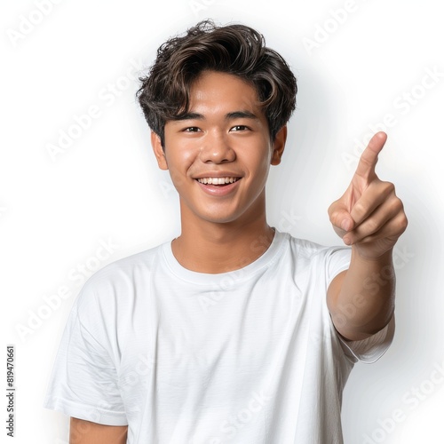 A cheerful handsome young Thai man wearing a white t-shirt points his finger with a white background.