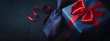 Blue gift box with red ribbon and tie on dark navy background, father day background