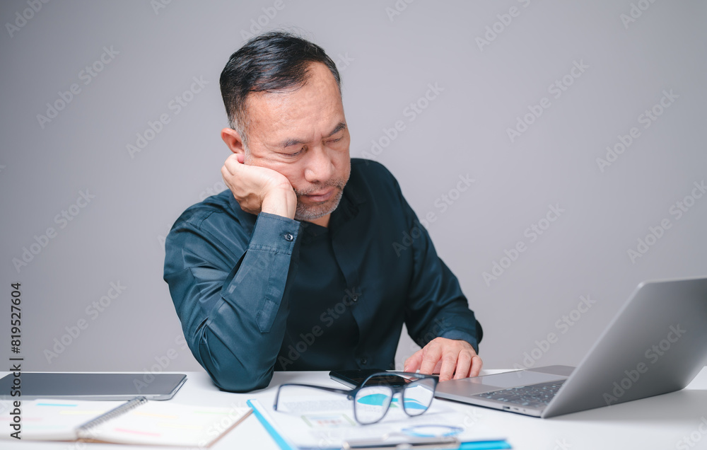 Sleepy businessman, an office manager, sits at his desk, working on his laptop, striving to stay productive despite his fatigue, highlighting relentless demands of his business responsibilities. Sleepy businessman, an office manager, sits at his desk, working on his laptop, striving to stay productive despite his fatigue, highlighting relentless demands of his business responsibilities.