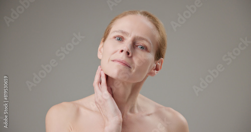 Anti age, Beauty, health and dry skin care concept - beautiful middle-aged mature Caucasian woman in her 50s touching her face skin and looking at the camera with a slight smile