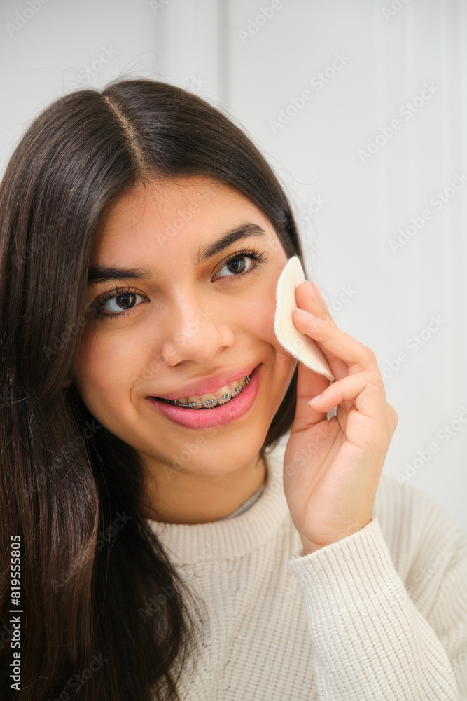 Female Latin teenager with braces using make up cotton pad. Female Latin teenager with braces using make up cotton pad.