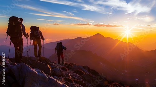 Three hikers watch the sun rise over a mountain range