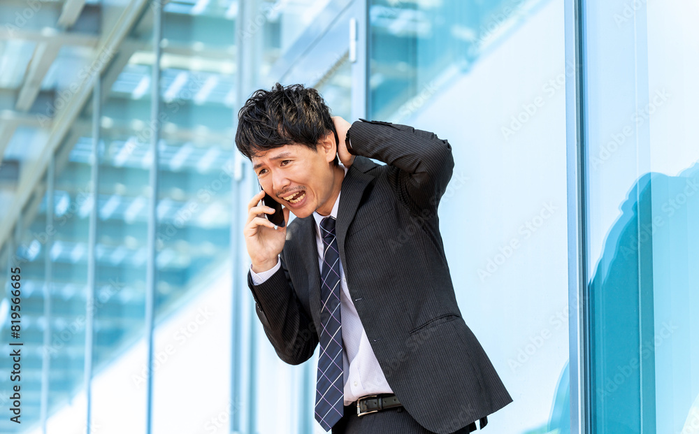 謝りながらスマホで話す男性ビジネスマン 謝りながらスマホで話す男性ビジネスマン