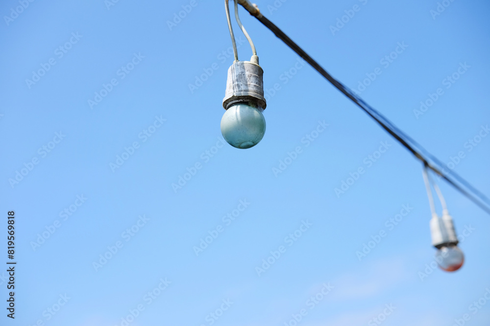 Equipped and electrical with light bulbs is hanging in the wind and sunlight on blue sky Equipped and electrical with light bulbs is hanging in the wind and sunlight on blue sky
