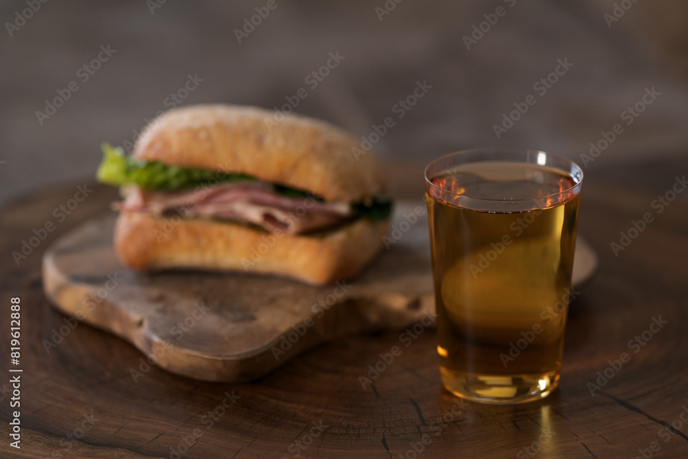 Ciabatta sandwich with ham and pesto and glass of cider on wood table Ciabatta sandwich with ham and pesto and glass of cider on wood table
