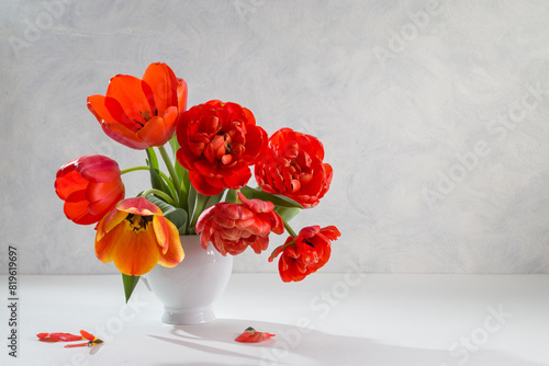A bouquet of red tulips in a white vase on a light background. Copy space