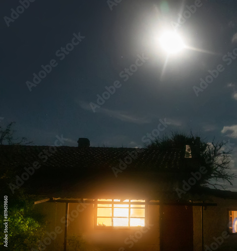 The fisherman's house, glowing window on a moonlit night is only a hundred meters from the seashore, midnight sky, southern rim photo