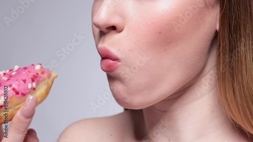 A young beautiful blonde girl eats a donut with pink icing and chocolate crumbs in a restaurant.