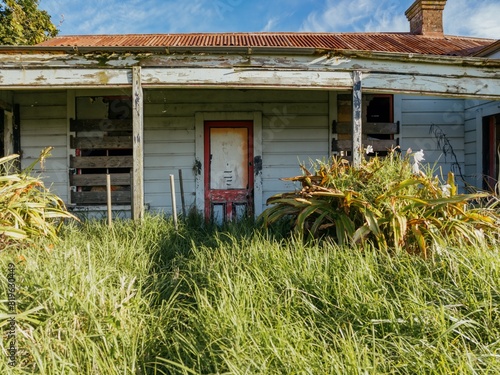 Abandoned and destroyed historic huse in overgrown grass in  Hāwera, Taranaki, New Zealand. photo