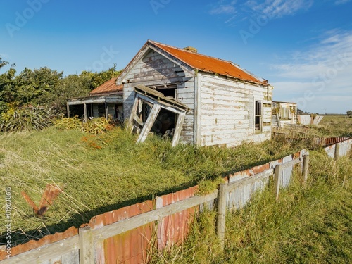 Abandoned and destroyed historic huse in overgrown grass in  Hāwera, Taranaki, New Zealand. photo