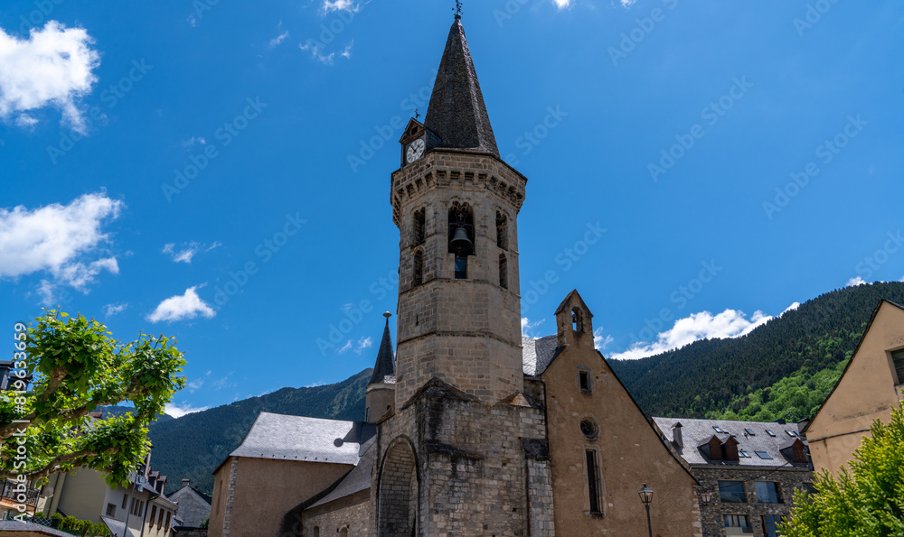 Fototapeta premium The town of Vielha in the Aran Valley, Lleida, Catalonia, Spain. The temple is in the center of the city, against a bright blue sky. Urban landscape in a mountain town.