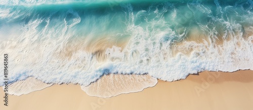 A view from above of a sandy beach with light blue water waves and sunlight a summer vacation background with a relaxation theme and room for text or images. Copy space image