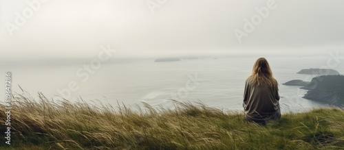 A teenage girl sitting on a grassy hill near the ocean in the Pacific Northwest on a misty day with a background suitable for a copy space image photo