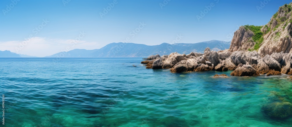 Fototapeta premium Scenic view with rocks in clear turquoise ocean green mountains in backdrop ideal for copy space image