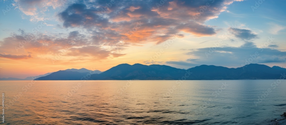 A picturesque sunset seascape with vibrant clouds hanging over the serene mountains and ocean perfect for use as a background in a copy space image
