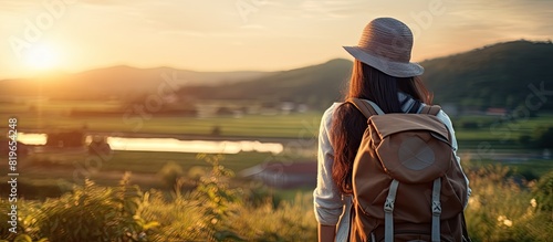 An Asian girl with a backpack is seen in nature at sunset embodying a relaxed holiday vibe with a hipster style color tone and selective focus on a copy space image #819654248