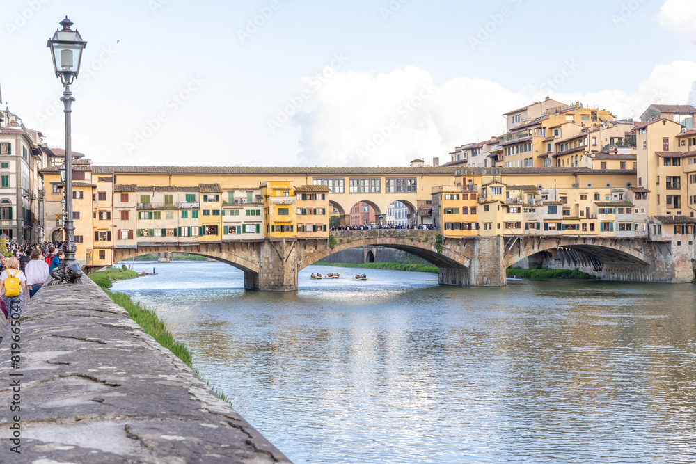 Obraz premium Florence, Italy - April 10, 2024: View of the Vecchio Bridge in Florence with tourists crowding its surroundings in Florence, Italy