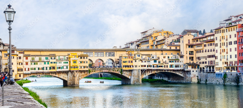 Fototapeta premium Florence, Italy - April 10, 2024: View of the Vecchio Bridge in Florence with tourists crowding its surroundings in Florence, Italy