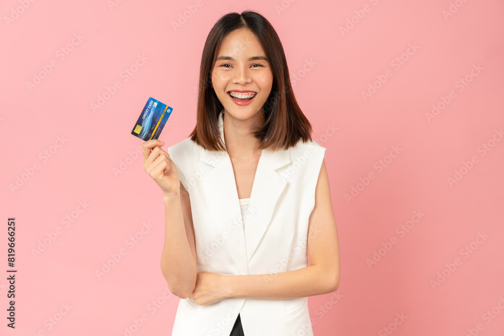 Naklejka premium Cheerful beautiful Asian woman holding mockup credit card on pink background.