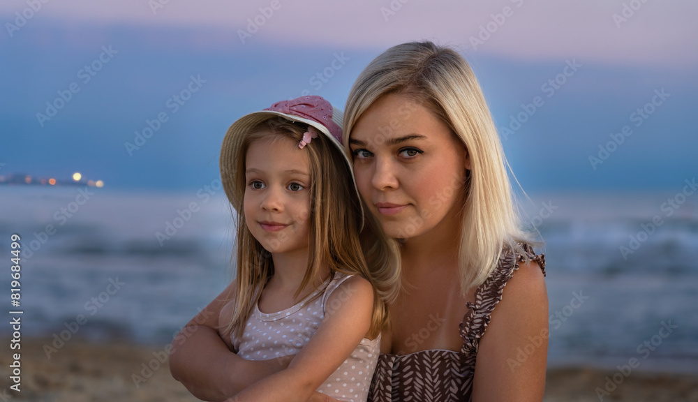 Close up of mother and daughter on beach of sea or ocean in evening at sunset. Happy family on summer vacation. Travel, holiday, tourism Close up of mother and daughter on beach of sea or ocean in evening at sunset. Happy family on summer vacation. Travel, holiday, tourism