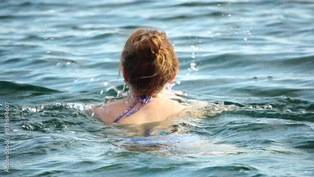 Woman swimming in calm sea at sunset, slow-motion, back view. Concept of body image and fitness, enjoying a serene beach. Happy woman with perfect fit body enjoys sea beach Woman swimming in calm sea at sunset, slow-motion, back view. Concept of body image and fitness, enjoying a serene beach. Happy woman with perfect fit body enjoys sea beach