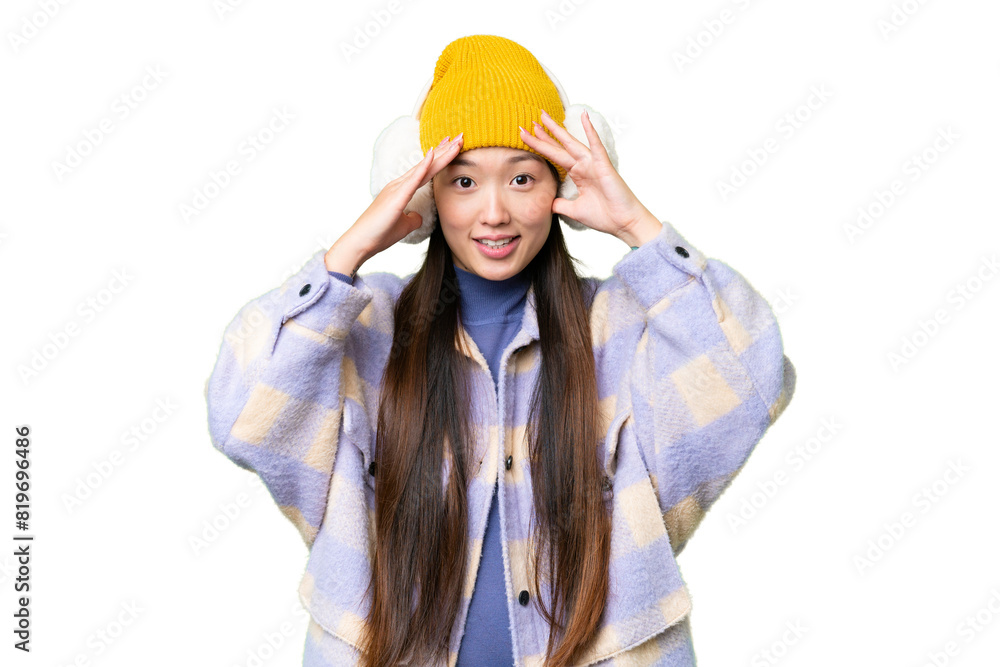 Young Asian woman wearing winter muffs over isolated chroma key background with surprise expression Young Asian woman wearing winter muffs over isolated chroma key background with surprise expression