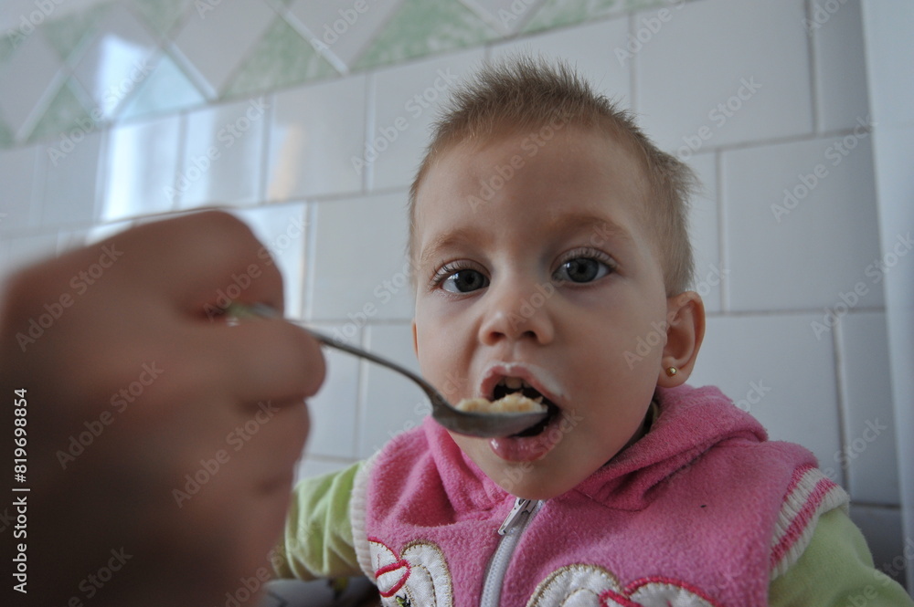 Mum feed the baby from a spoon, close-up. A child who has one year eats porridge. First teeth