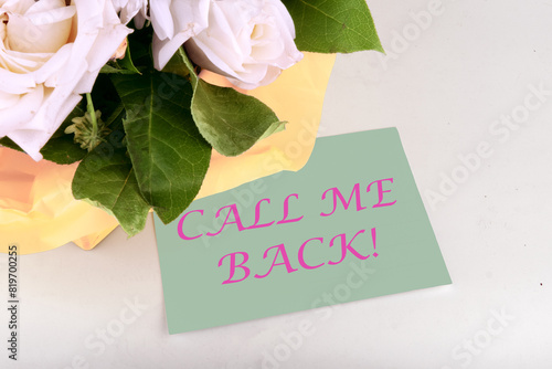 CALL ME BACK text written on a piece of paper near a bouquet of flowers