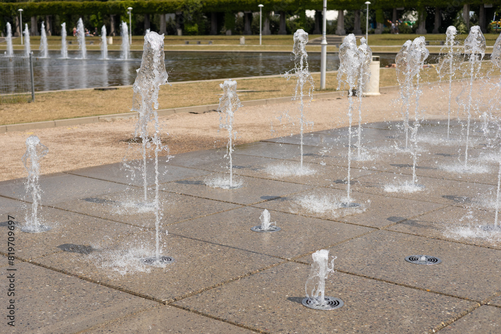 Water droplets spread from the fountain in the air. Splashing water from a fountain in the park. Vertical fountain jets in the sidewalk on the square in the city park.