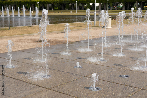 Obraz na płótnie Water droplets spread from the fountain in the air. Splashing water from a fountain in the park. Vertical fountain jets in the sidewalk on the square in the city park. w salonie