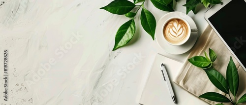 Minimalist white surface with notepad, coffee, tablet, and green leaves