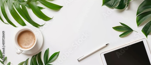 Minimalist workspace items notepad, coffee, tablet, and green leaves on white photo