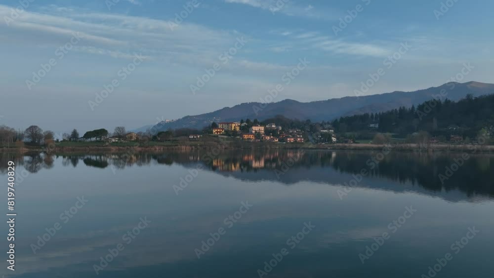 Drone of the reflection of houses in green field on the Lake Montorfano, with mountain behind them Drone of the reflection of houses in green field on the Lake Montorfano, with mountain behind them