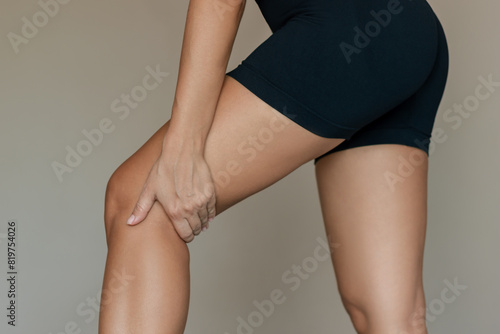 Cropped shot of a young woman standing in profile touching painful popliteal fossa with hand. Sport injury, sore knee joint. Acute pain in the back of the knee. Popliteal tendinitis. Medical concept photo