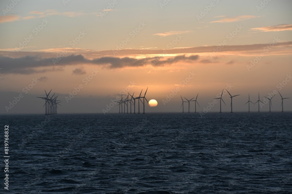 Breathtaking view of wind turbines seen from the sea against a cloudy sunset sky Breathtaking view of wind turbines seen from the sea against a cloudy sunset sky