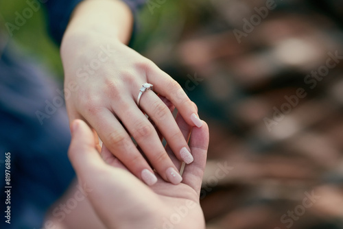 Couple, engagement ring and nature with holding hands in closeup for proposal with love, surprise and commitment. Man, woman and vacation with jewelry, question and marriage offer in countryside