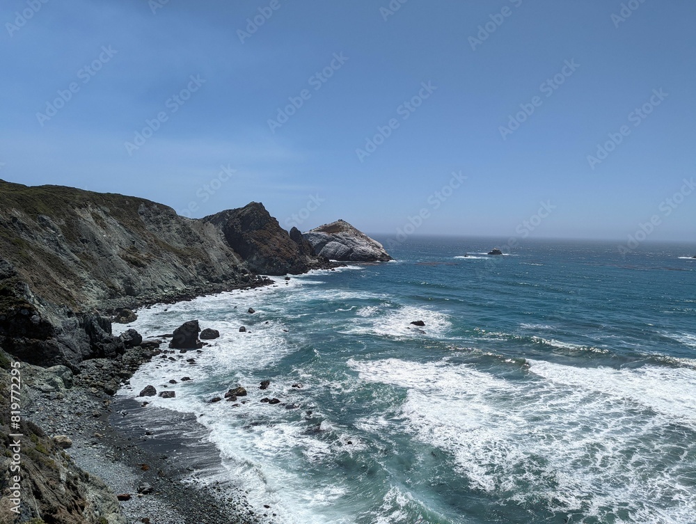 Foamy waves of an ocean hitting the rocks on the shore with the horizon in the sunny background Foamy waves of an ocean hitting the rocks on the shore with the horizon in the sunny background