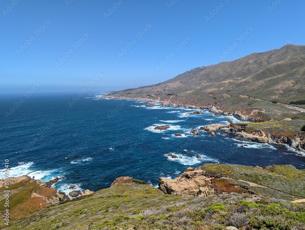 Obraz premium Foamy waves of an ocean hitting the rocks on the shore with the horizon in the sunny background