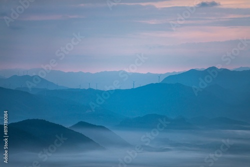 Drone shot of silhouettes of green-covered hills in mist at sunset, cool for background