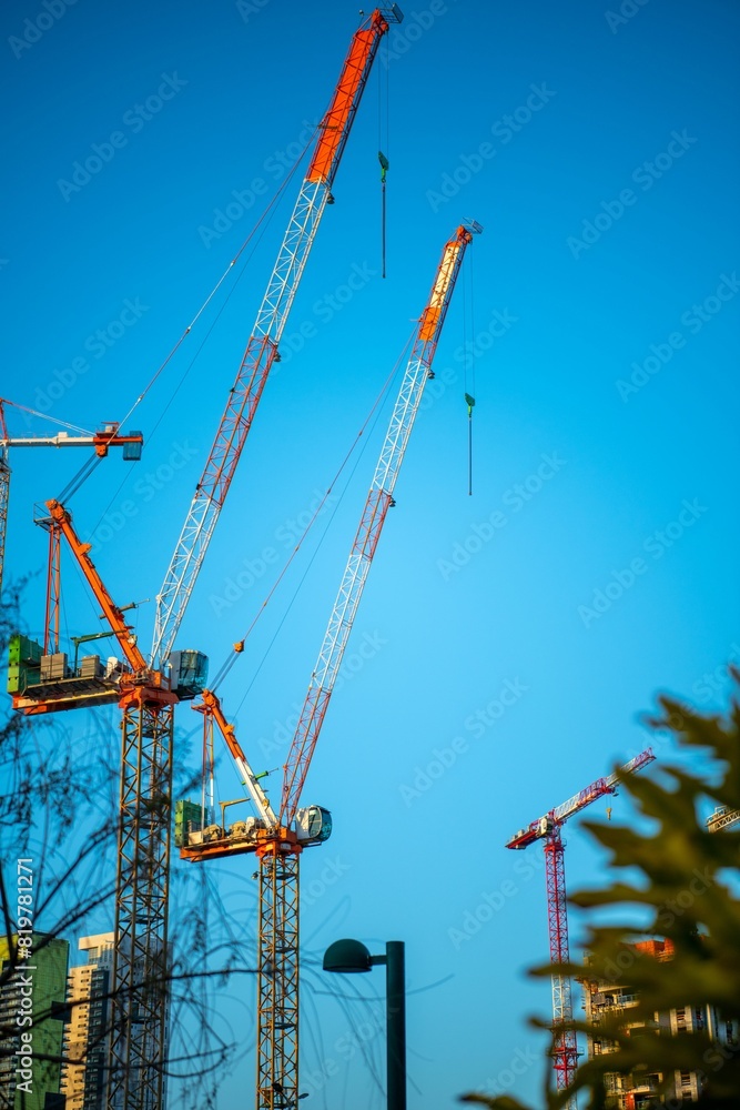 Cityscape featuring multiple cranes suspended in the blue sky. Cityscape featuring multiple cranes suspended in the blue sky.