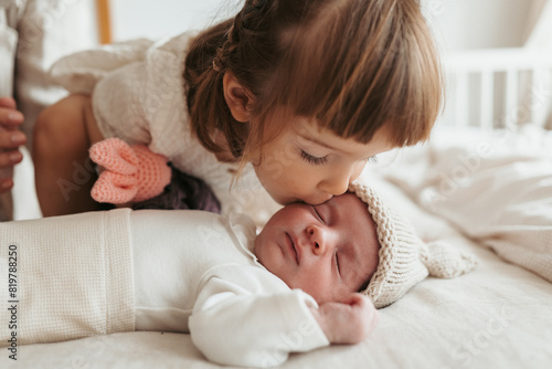 Toddler sister giving a gentle kiss to her sleeping newborn brother photo